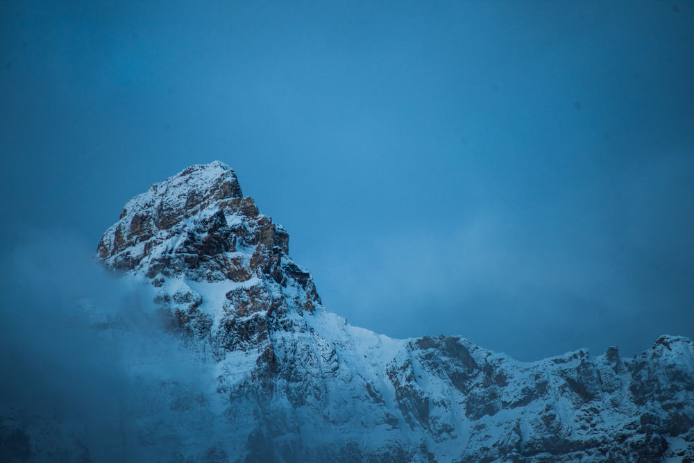 clouds creep over snowy mountain