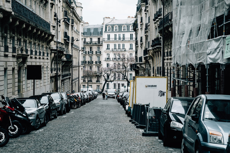 Cobblestone Street With Tall Buildings And Cars