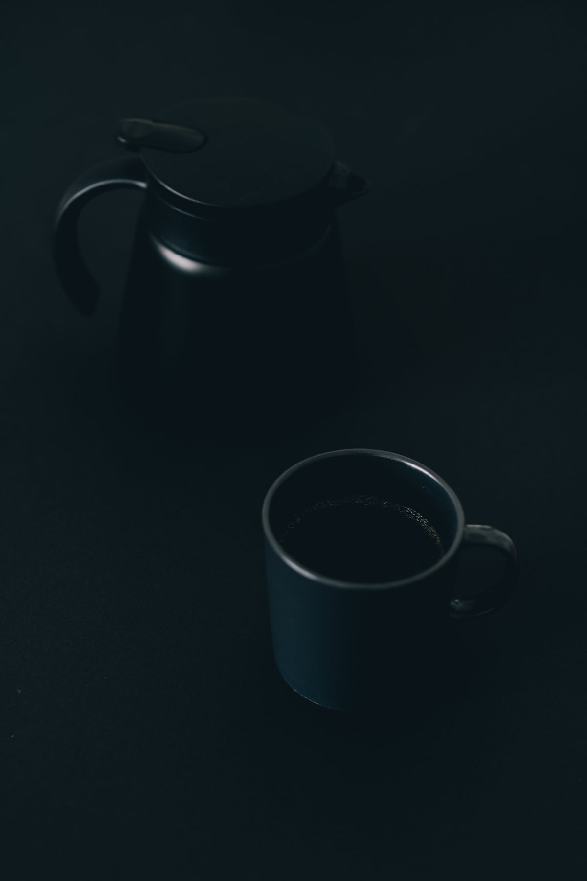 coffee mug and pot sitting on a black surface