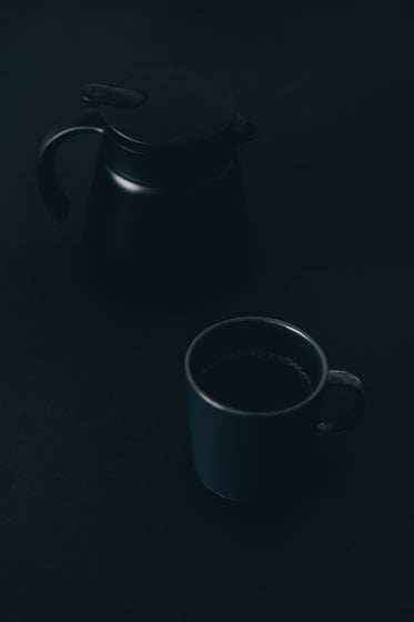 coffee mug and pot sitting on a black surface