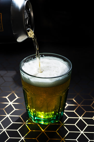 cold drink pours from a silver can into a glass with a green tint