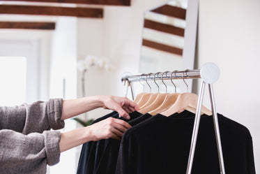 comparing black t-shirts on a clothing rack in a sun-lit shop