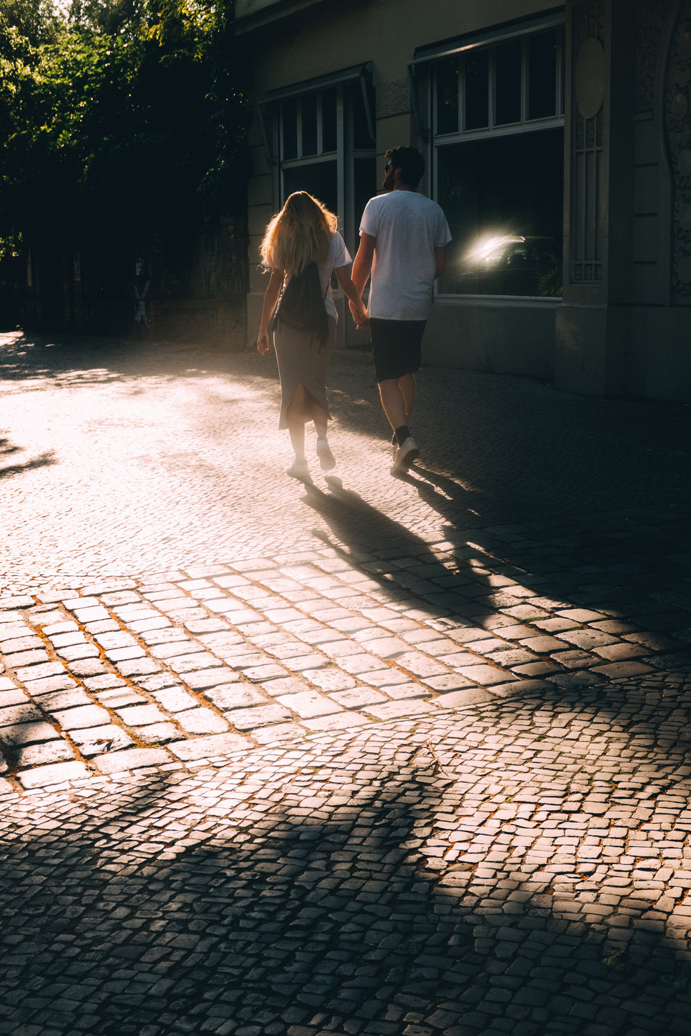 couple holds hands and walks on stone sidewalk