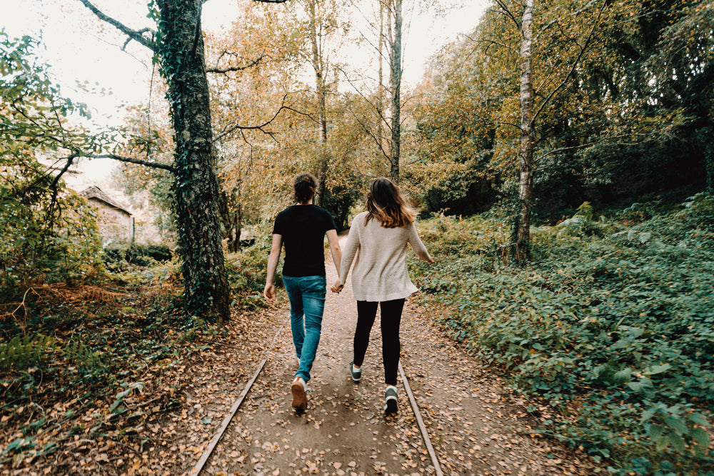 couple holds hands walking through green and yellow trees