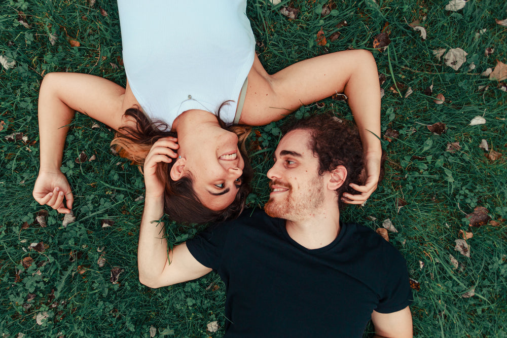 couple lays on grassy field looking at each other and smiling