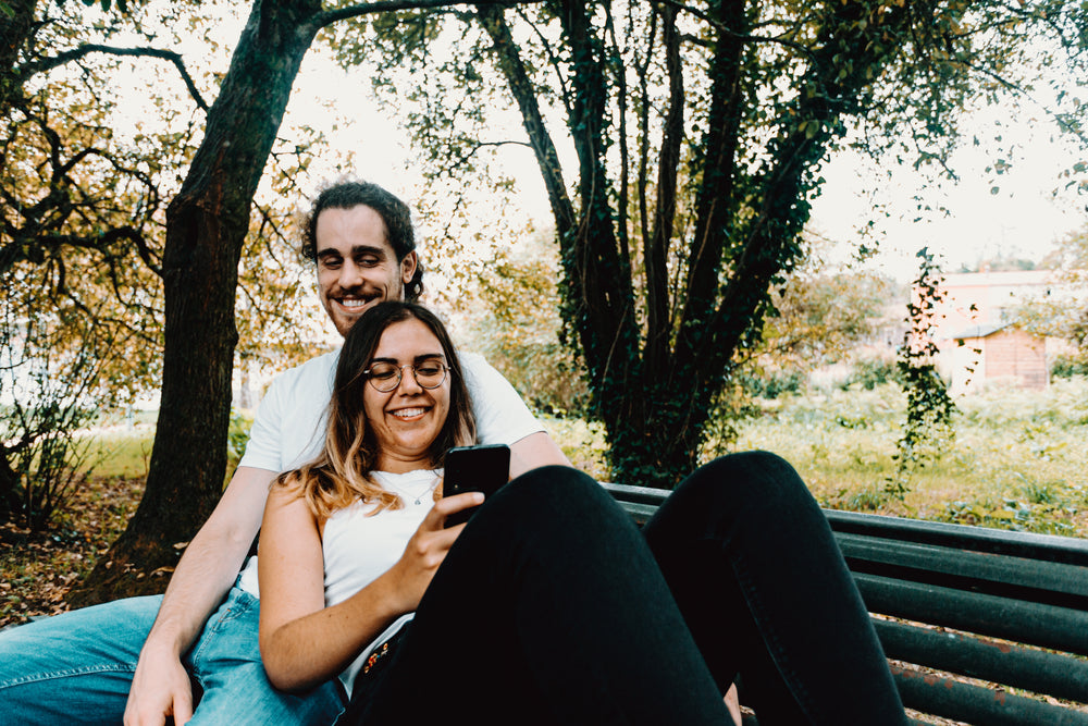 couple on a park bench and look at a cell phone