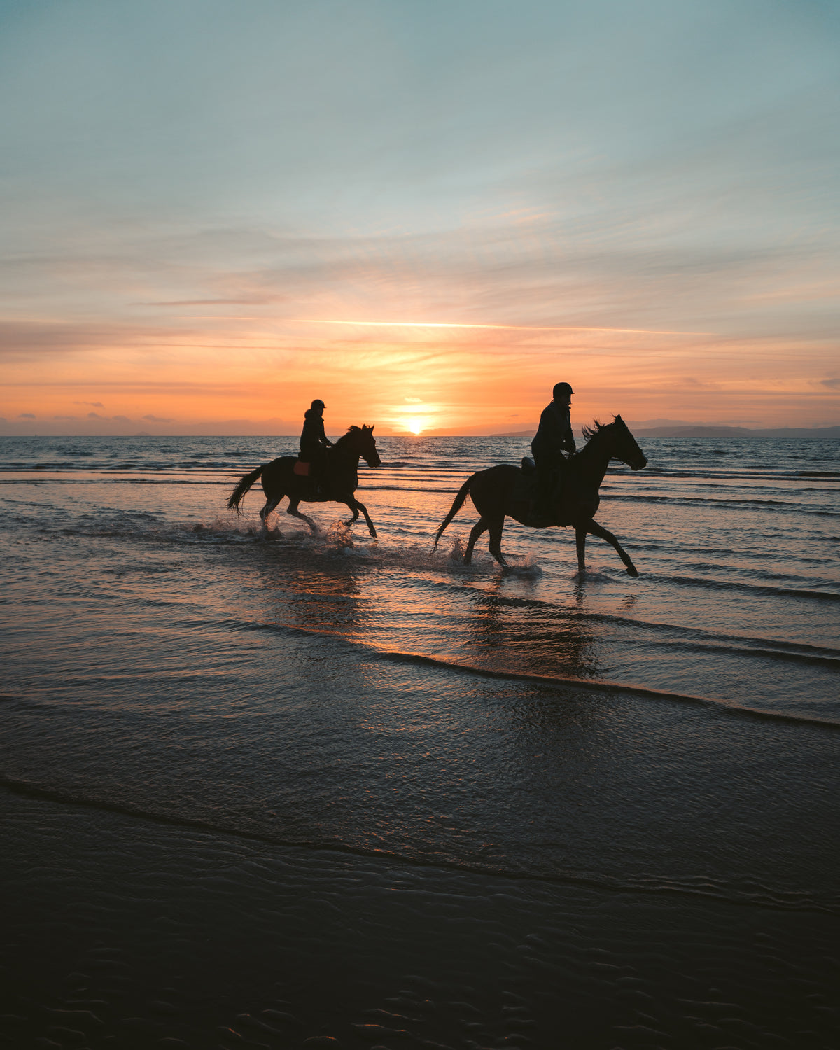 一对情侣在日落的海滩上骑马