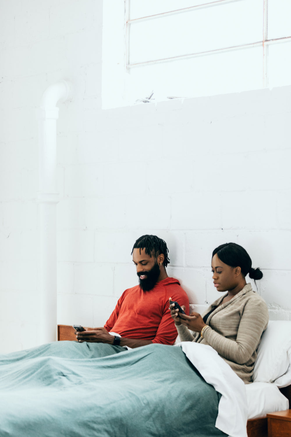 couple sits in bed and looks at their phones