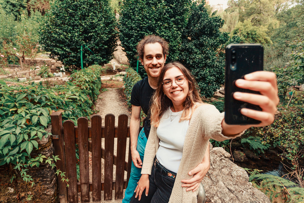 couple smile at a cell phone while standing outdoors