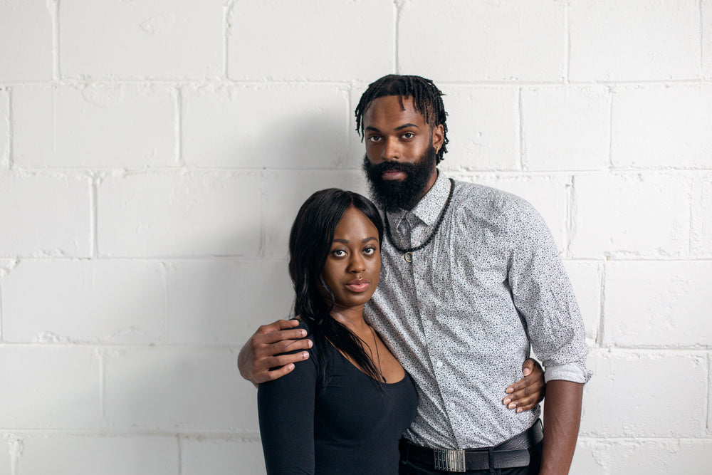 couple stand against white wall looking at camera
