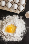 cracked egg resting in well of flour on black counter