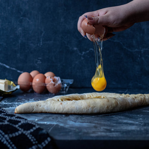 cracking an egg above fresh dough on marble surface