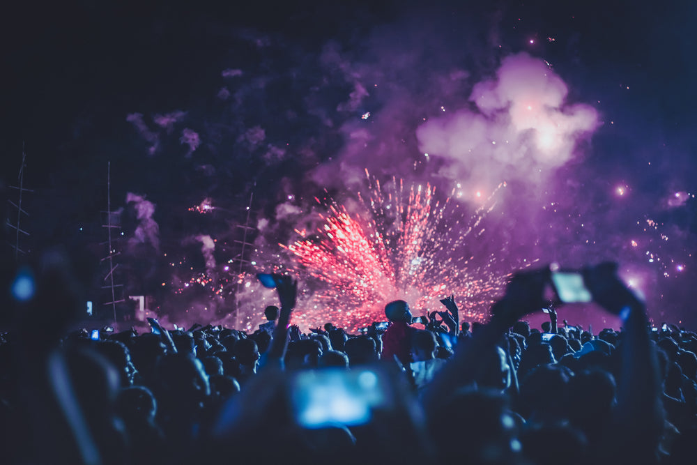 crowd watching pink fireworks erupting into clouds of purple