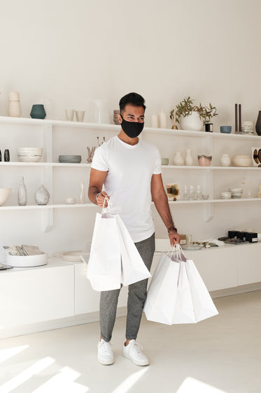 customer in face mask smiles and holds white shopping bags