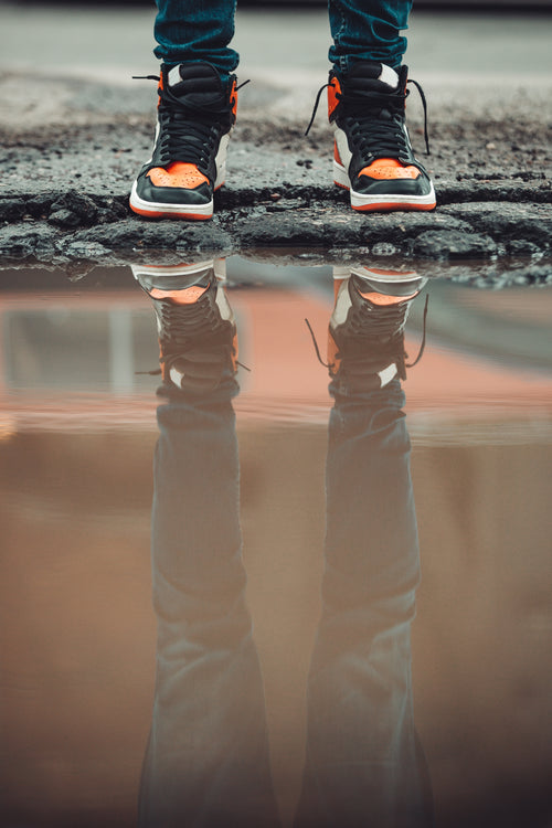 dark denim jeans and fashion sneakers reflect in city puddle