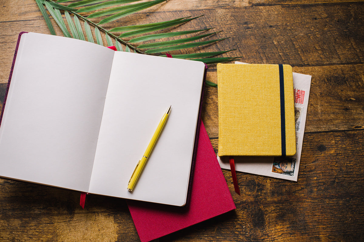 深色木桌，桌上有笔记本、树叶和一支黄色钢笔