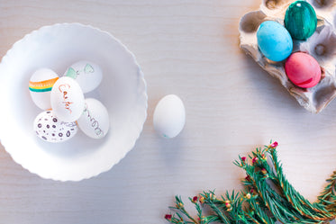 decorated easter eggs in a white bowl and egg carton