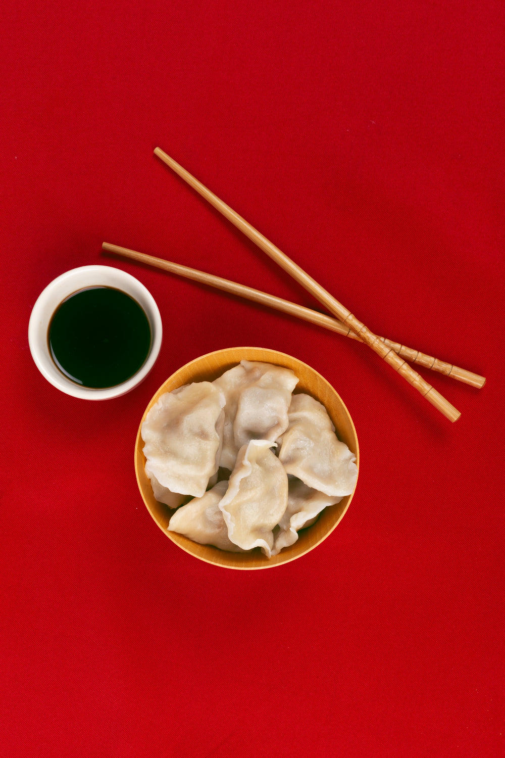 dumplings chopsticks and sauce on a red cloth viewed from above