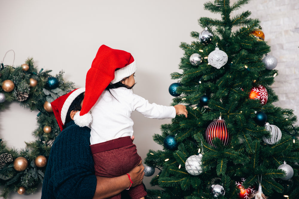 father helps toddler decorate christmas tree