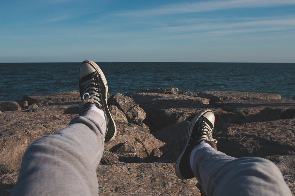 feet in sneakers pointed towards open ocean off rocky shore