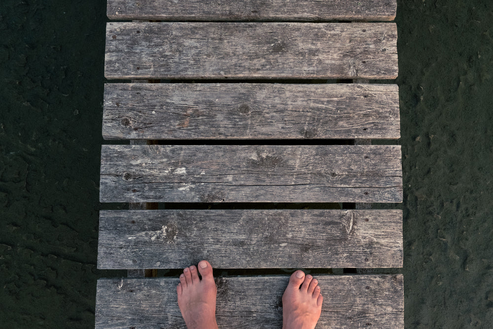 feet on a dock over rocky sandy ground