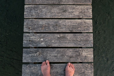 feet on a dock over rocky sandy ground