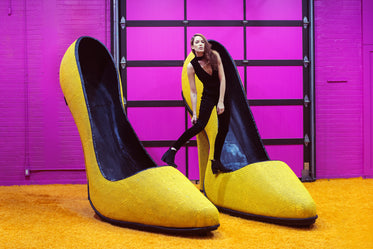 female model perches atop giant yellow high heel shoes