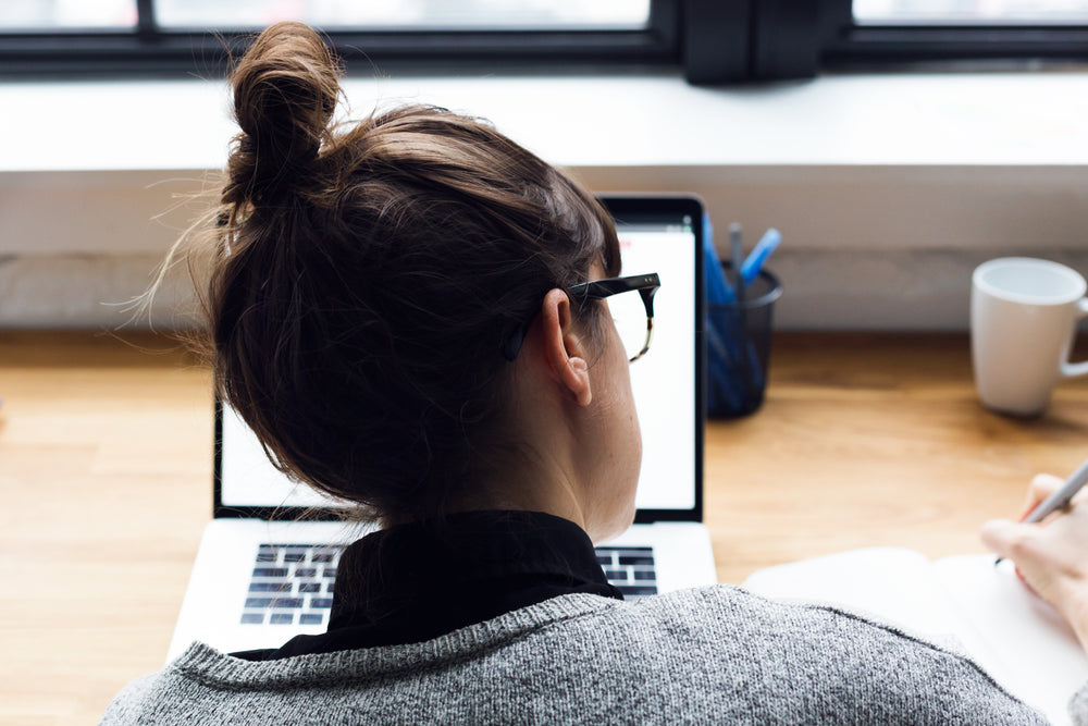 mulher faz anotações e pesquisa no laptop