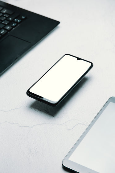 flatlay of a cell phone floating with laptop and tablet