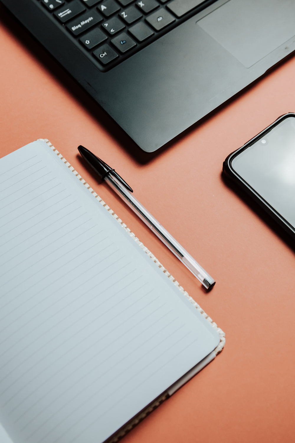 flatlay of a notebook pen laptop and cellphone