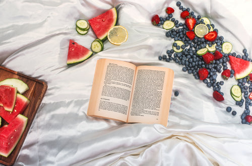 flatlay of a open book surrounded by fresh fruit on white silk
