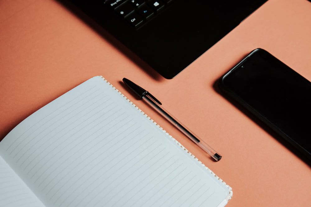 flatlay of a pen next to paper and a laptop and cellphone