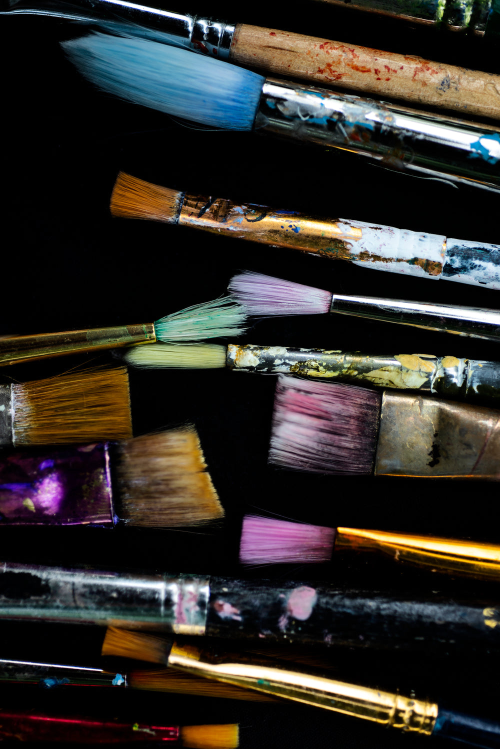 flatlay of dyed paint brushes laying on black surface