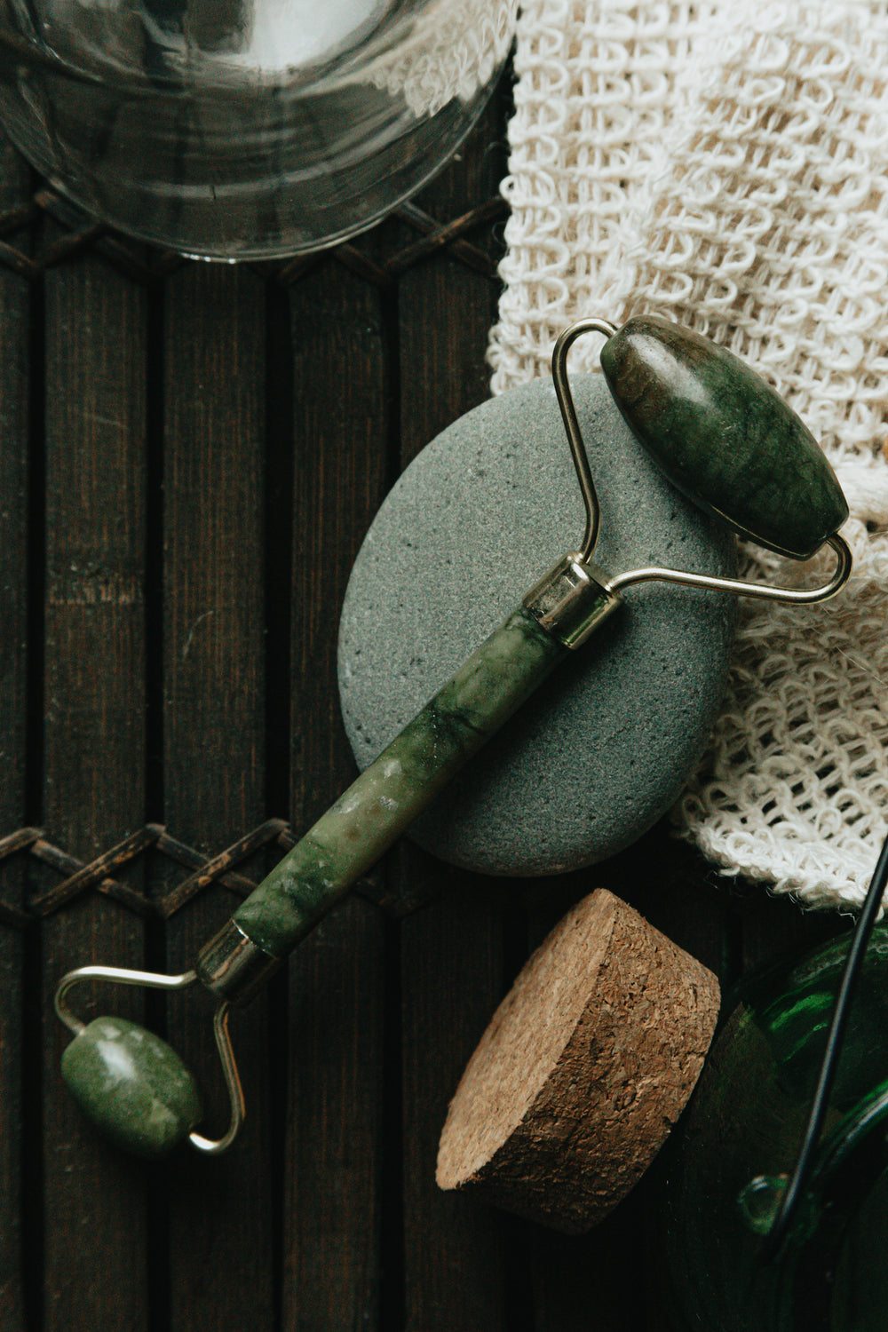 flatlay of jade face roller laying on a grey stone