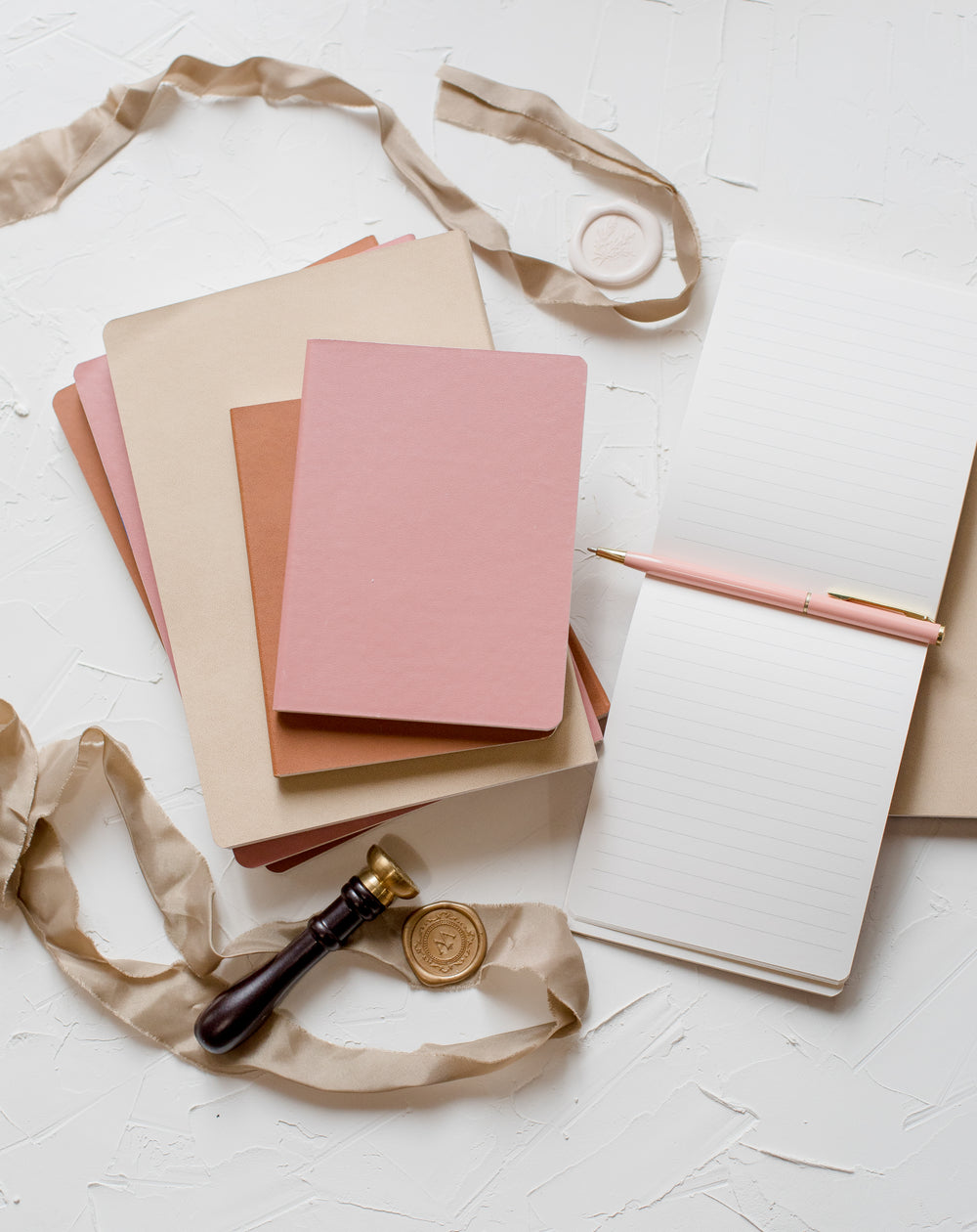 flatlay of notebooks a ribbon and a wax seal