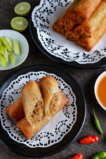 flatlay of plated spring rolls with hot peppers and limes