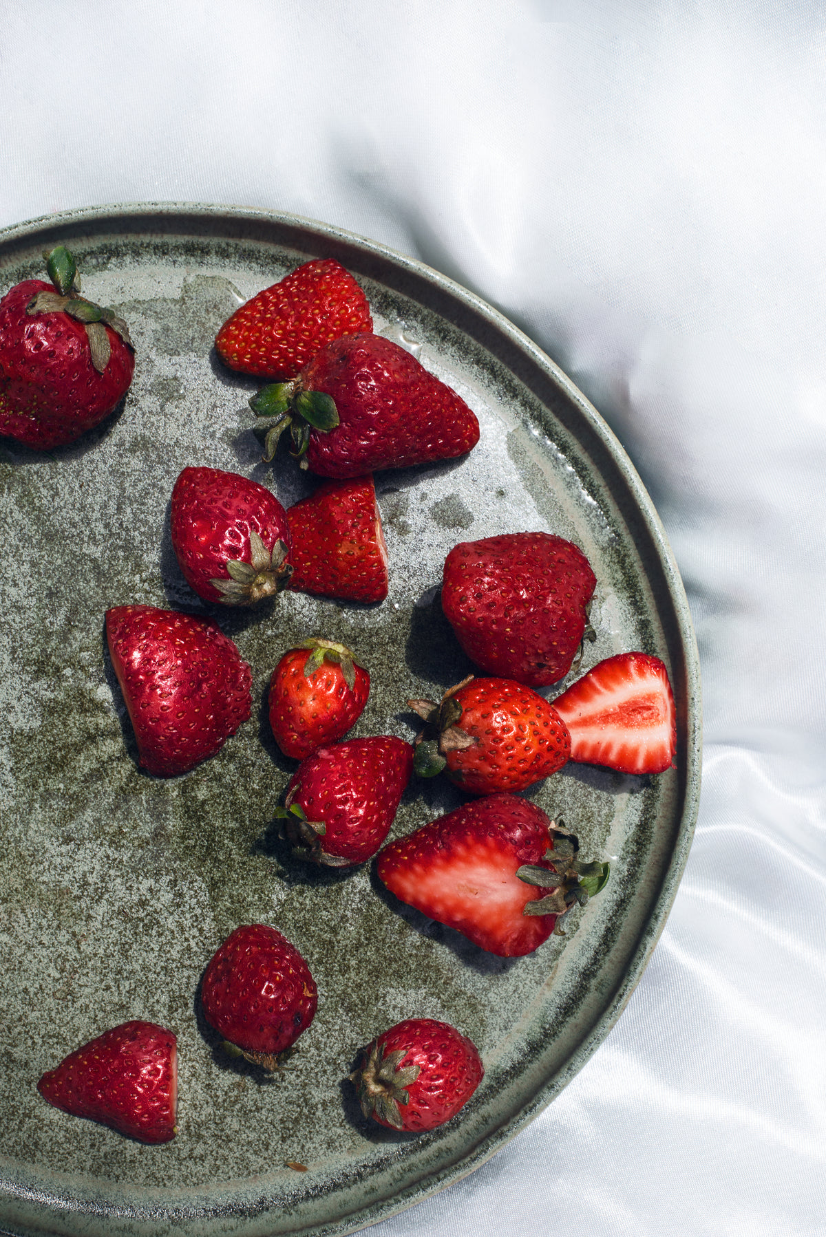 flatlay of ripe strawberries on a green plate on silk