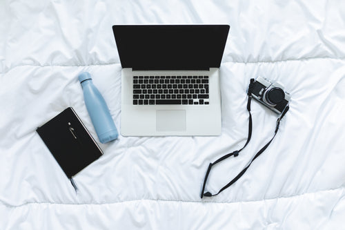 flatlay on a bed with notebook laptop and camera