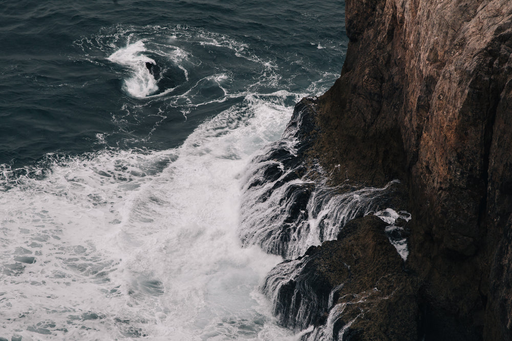 foamy waves claw at the base of a cliff