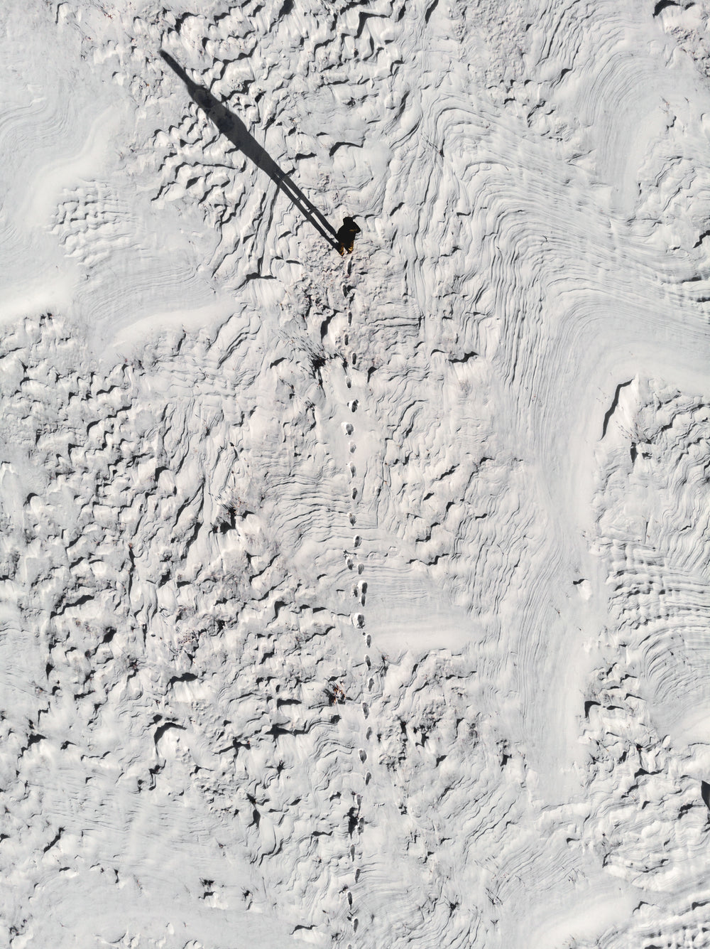 footprints in wind carved snowscape lead to human silhouette