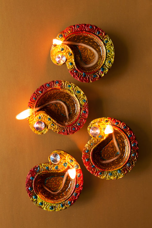 four candlelit diya lamps rest on brown background