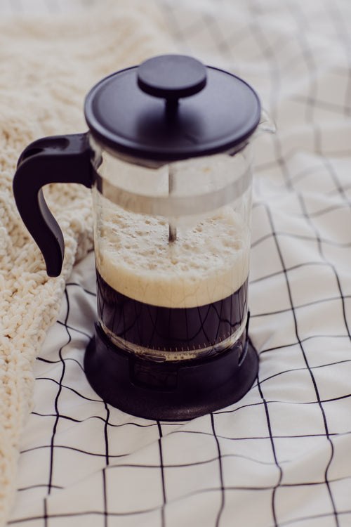 french press with frothy black coffee on white blanket