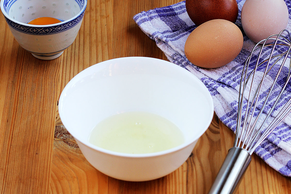 fresh eggs being separated into white bowl with whisk