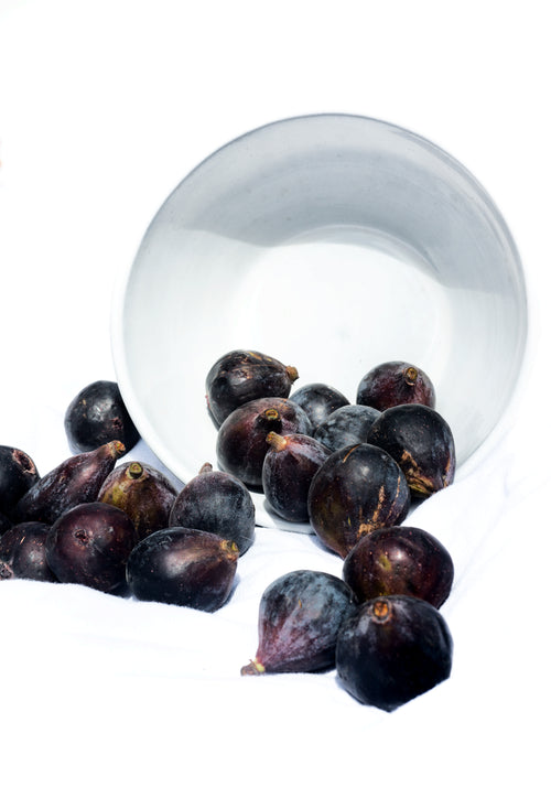 fresh fig fall out of a white bowl onto a blanket