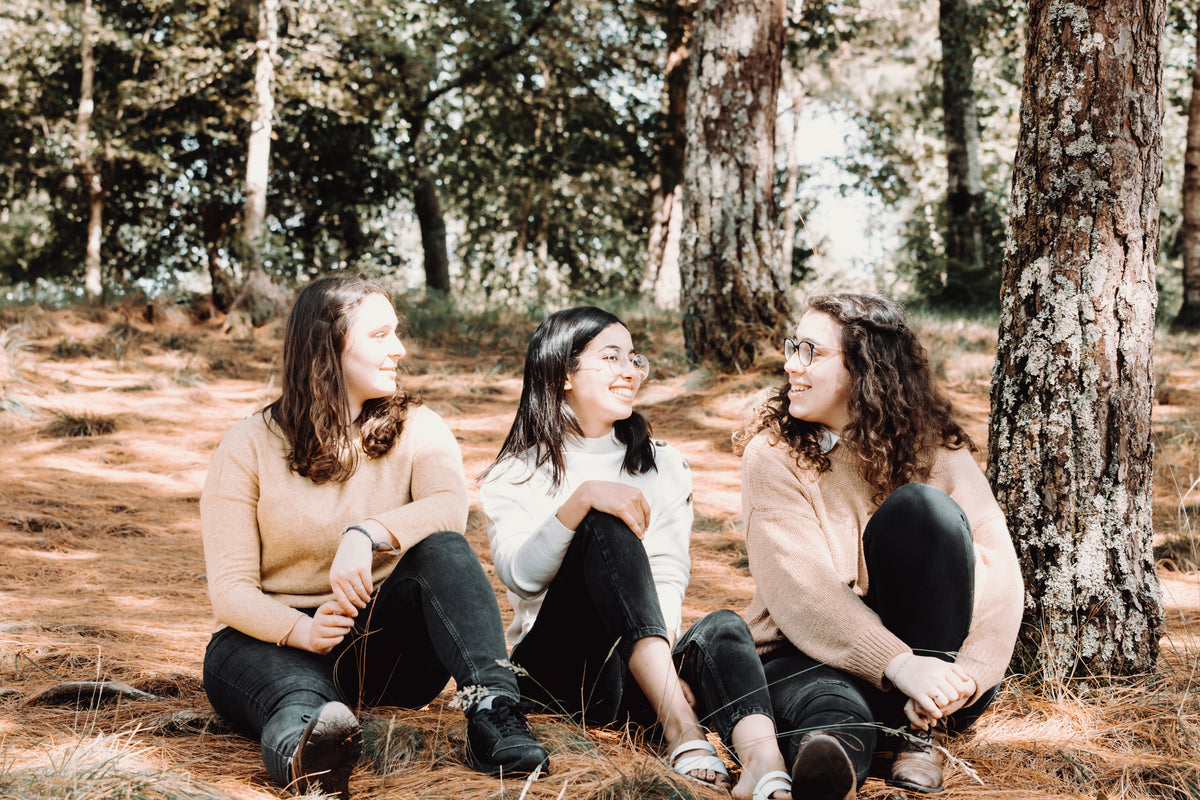 friends in sweaters chat under large trees in a forest