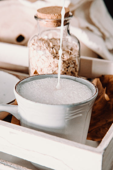 frothy milk pouring into a ceramic mug on wooden tray