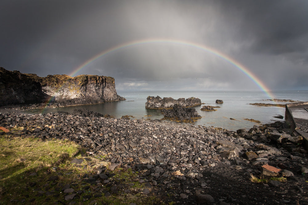 full rainbow over rocks and water