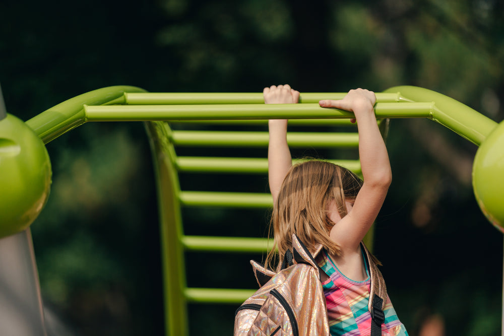 girl swinging on bars with backpack