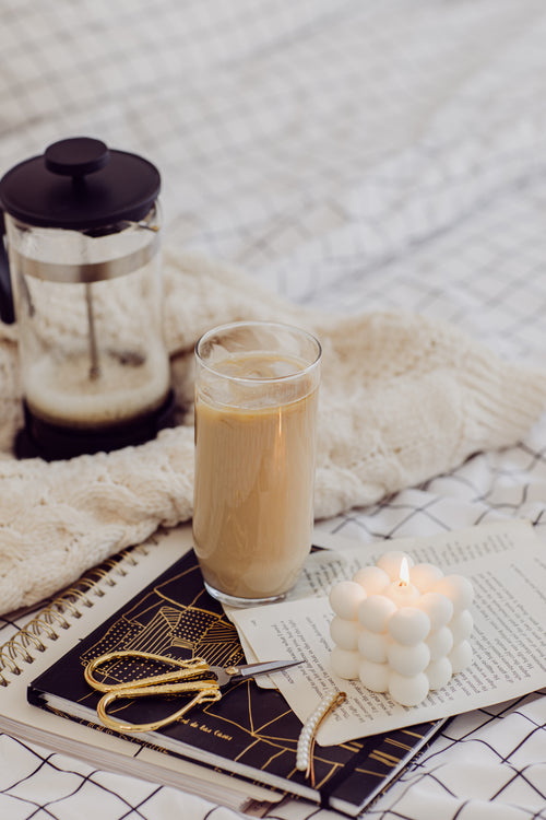 glass iced coffee a notebook and lit candle on a bed sheet