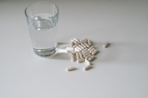 glass of water and pills on a white countertop